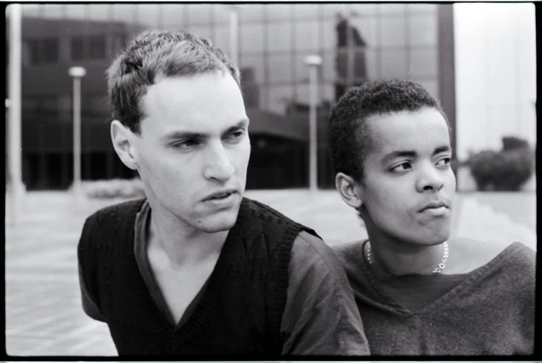 Zwei junge Männer schauen auf der Schwarz-Weiß-Aufnahme in die Ferne. Sie sitzen eng beieinander.