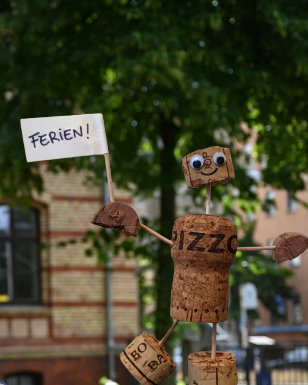 Ein Korkmännchen hält eine Fahne mit der Aufschrift "Ferien!".